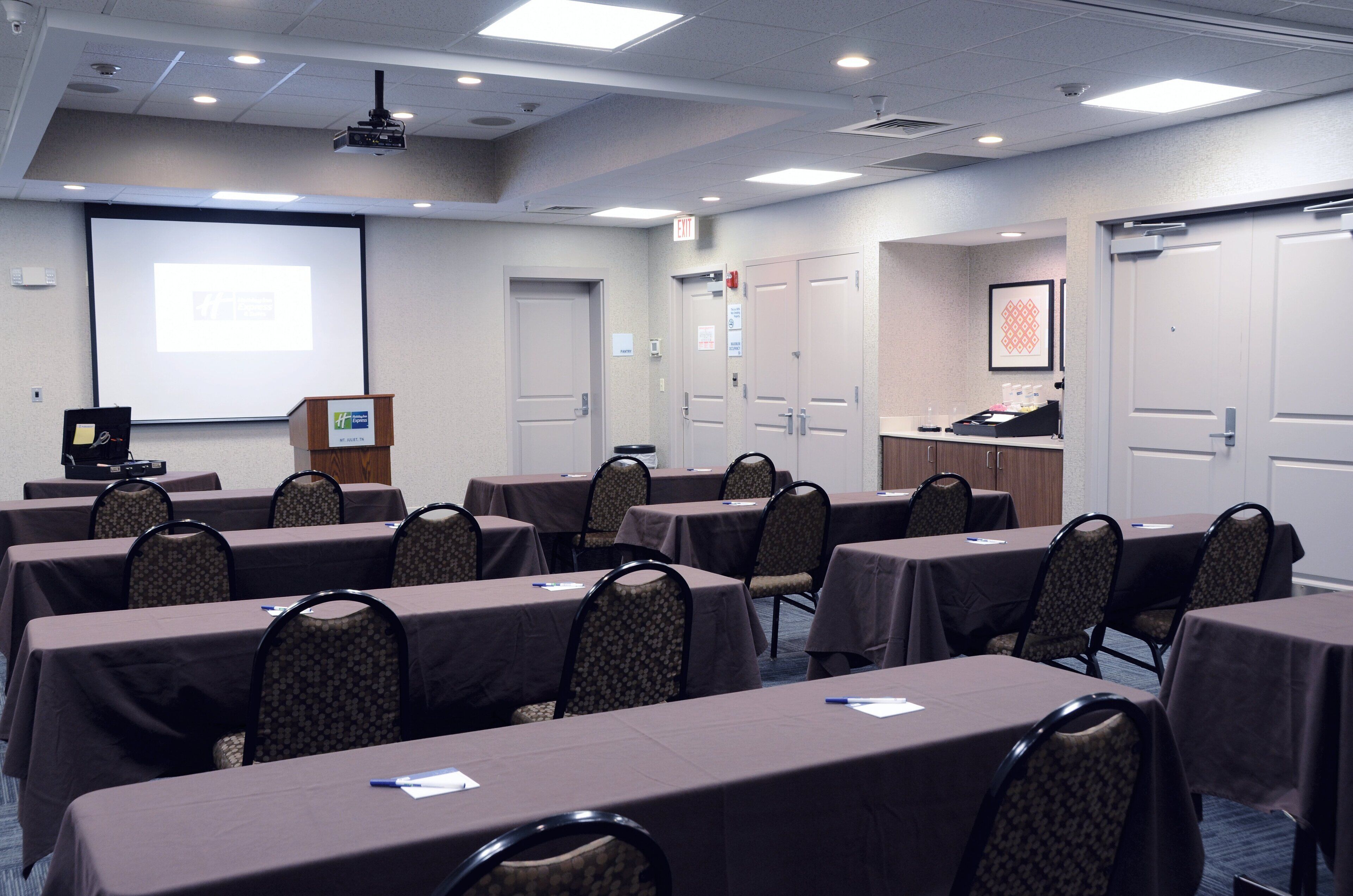 A conference room with tables, chairs, a projector screen, and a presentation podium.