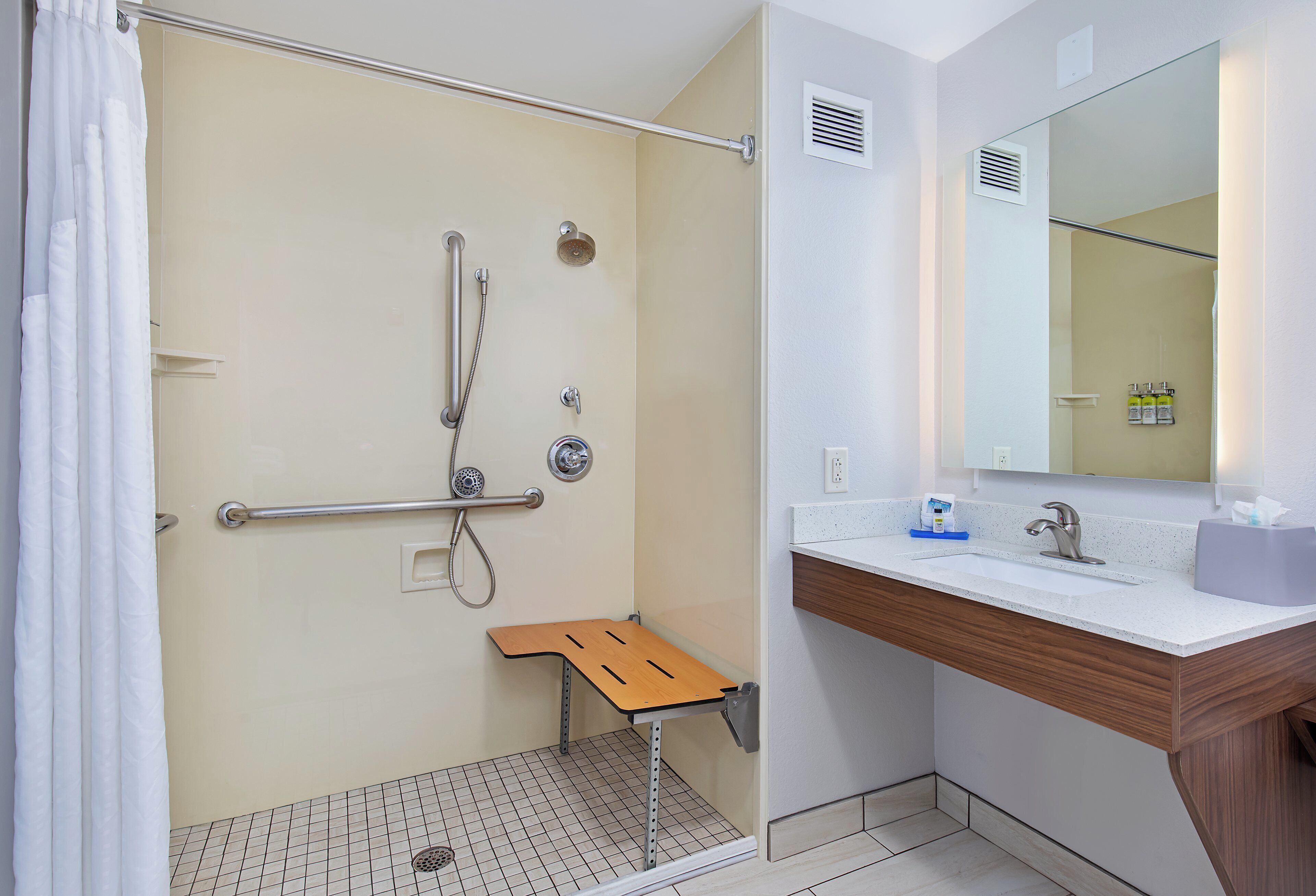 A bathroom with a shower, a sink, a mirror, and a small wooden stool.