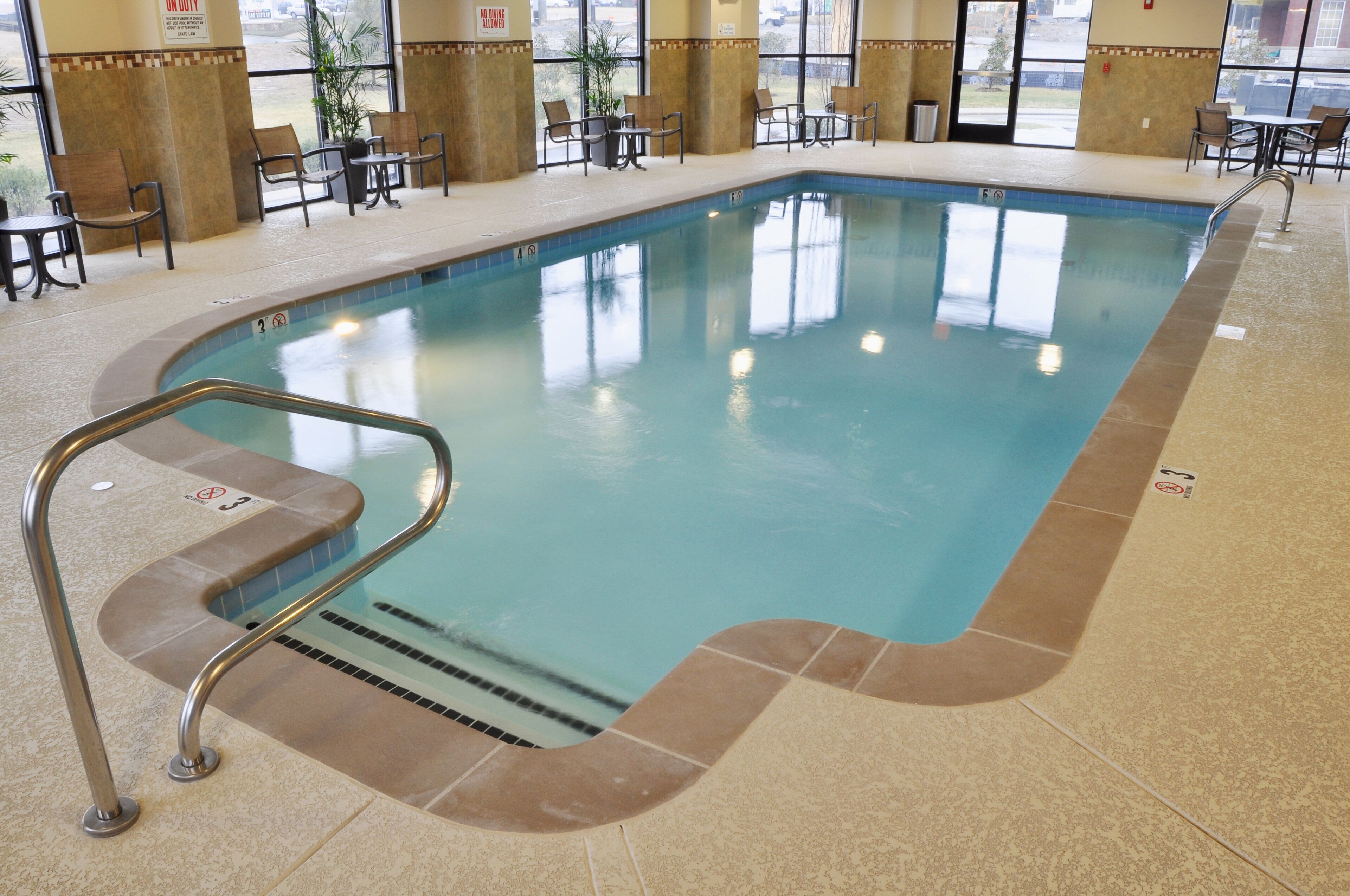 Una piscina interior con borde de azulejos, una escalera metálica y suelo de baldosas.