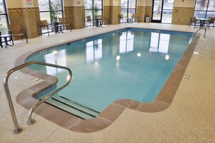Una piscina interior con borde de azulejos, una escalera metálica y suelo de baldosas.