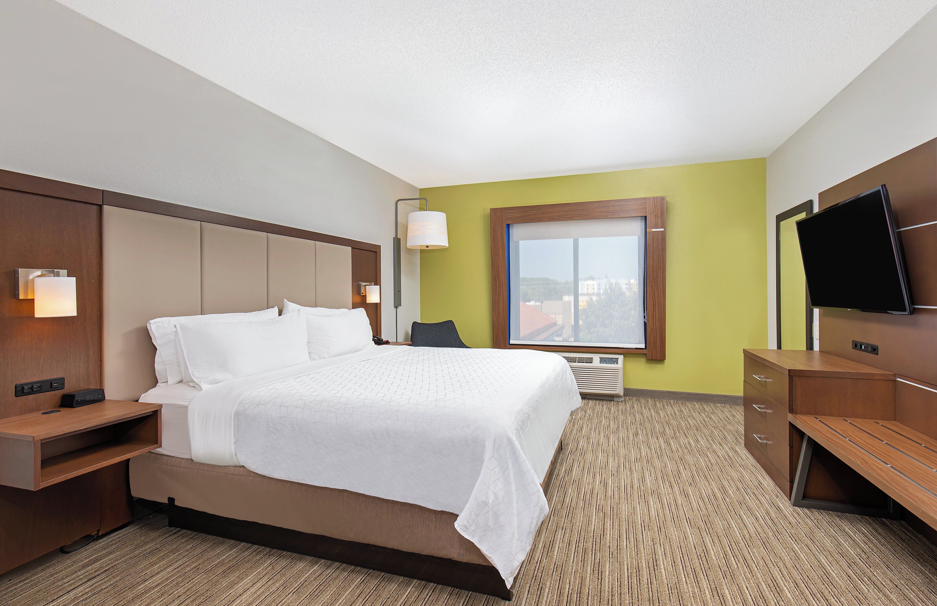 Ein Hotelzimmer mit Bett, Nachttischen, Fernseher, Fenster und einer Wandlampe.