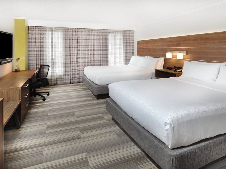 Habitación de hotel con dos camas, un escritorio, una silla, un televisor y una ventana con cortinas.