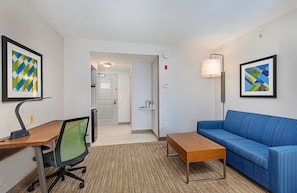A hotel room with a desk, office chair, blue sofa, and two framed artworks on the walls.