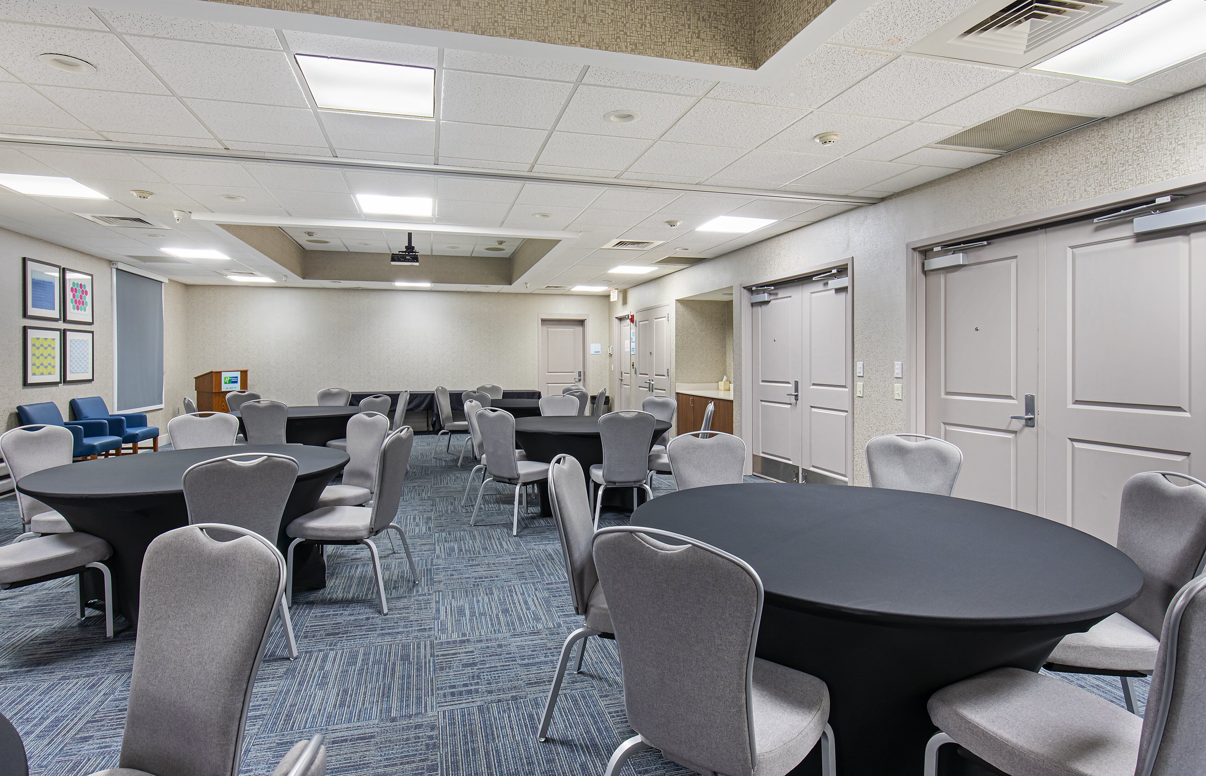 A conference room with multiple tables and chairs, a carpeted floor, and a ceiling with recessed lighting.