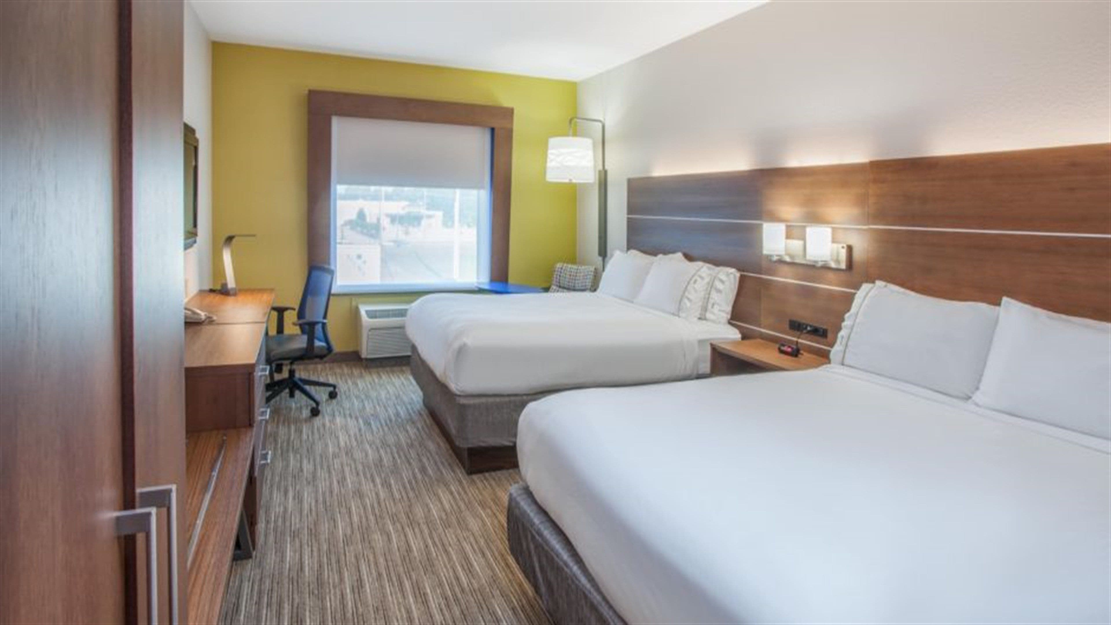 A hotel room with two beds, a desk, a chair, a window with a view, and a lamp.