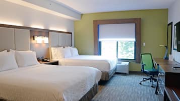 A hotel room with two beds, a desk with a chair, a window with a view, and a wall-mounted air conditioning unit.