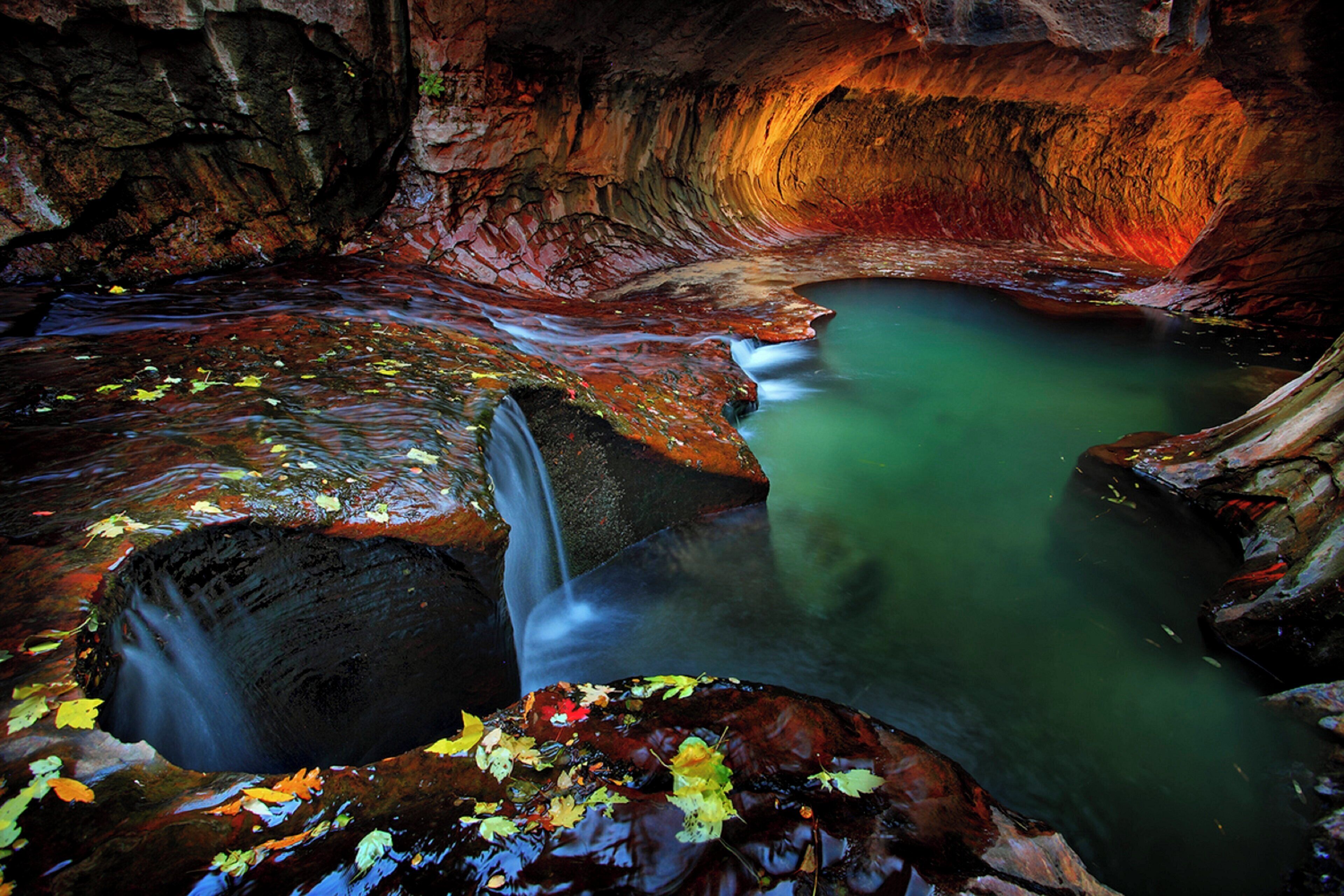 A natural cave waterfall with clear water and surrounding rock formations.