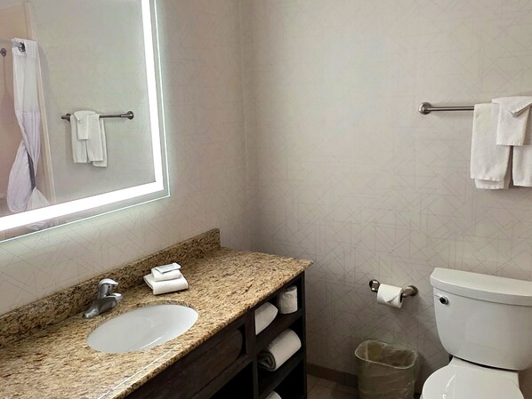 Un baño con lavamanos de encimera de granito, un espejo, inodoro y barra para toallas.