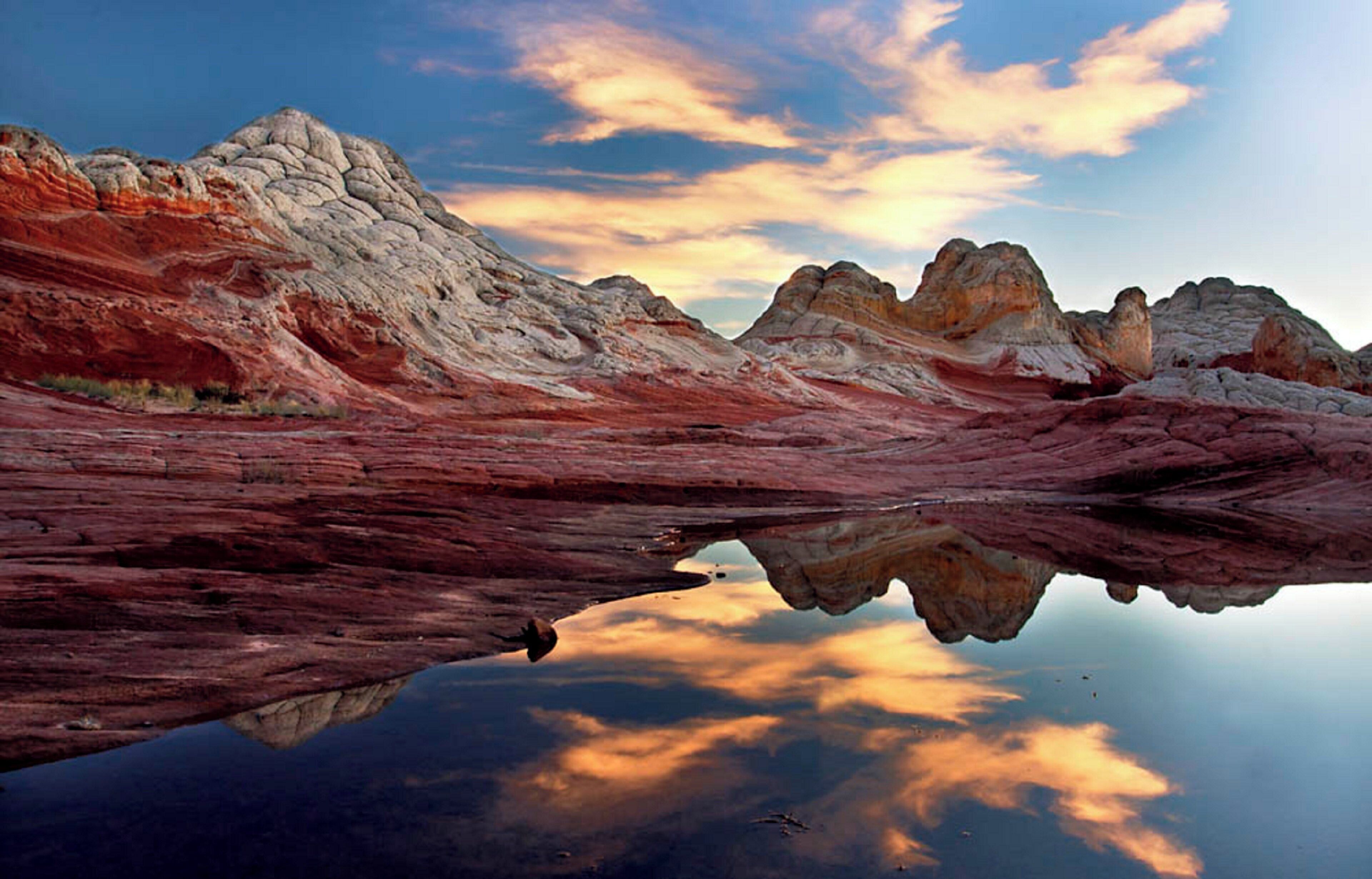 A landscape with a reflective body of water, rocky terrain, and a clear sky.
