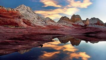 A landscape with a reflective body of water, rocky terrain, and a clear sky.