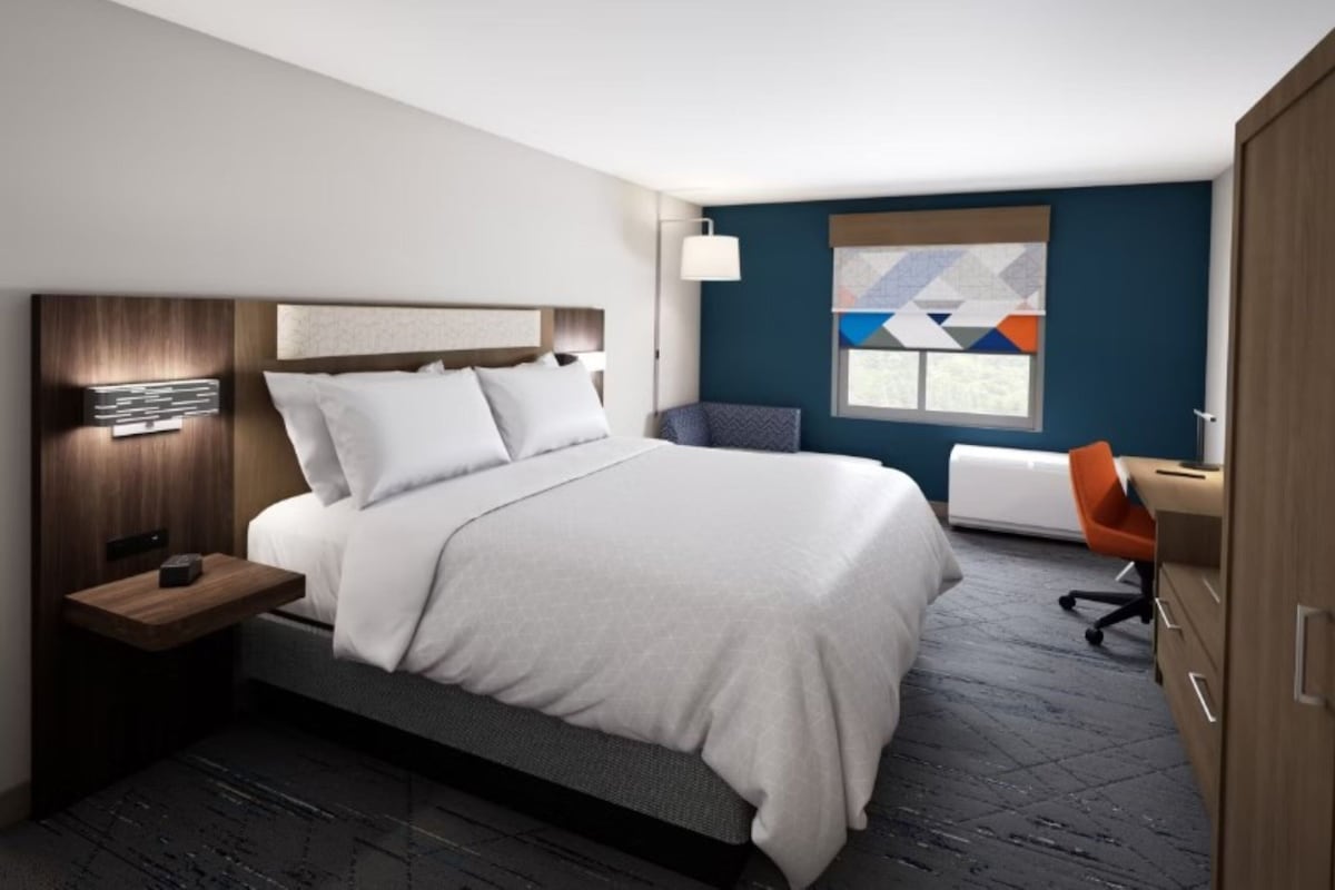 A modern hotel room with a large bed, a desk, and a chair.
