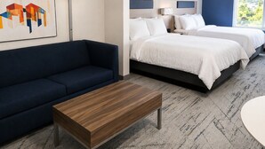 Une chambre d’hôtel avec un canapé, deux lits, une table de chevet, une lampe et un tableau au mur.