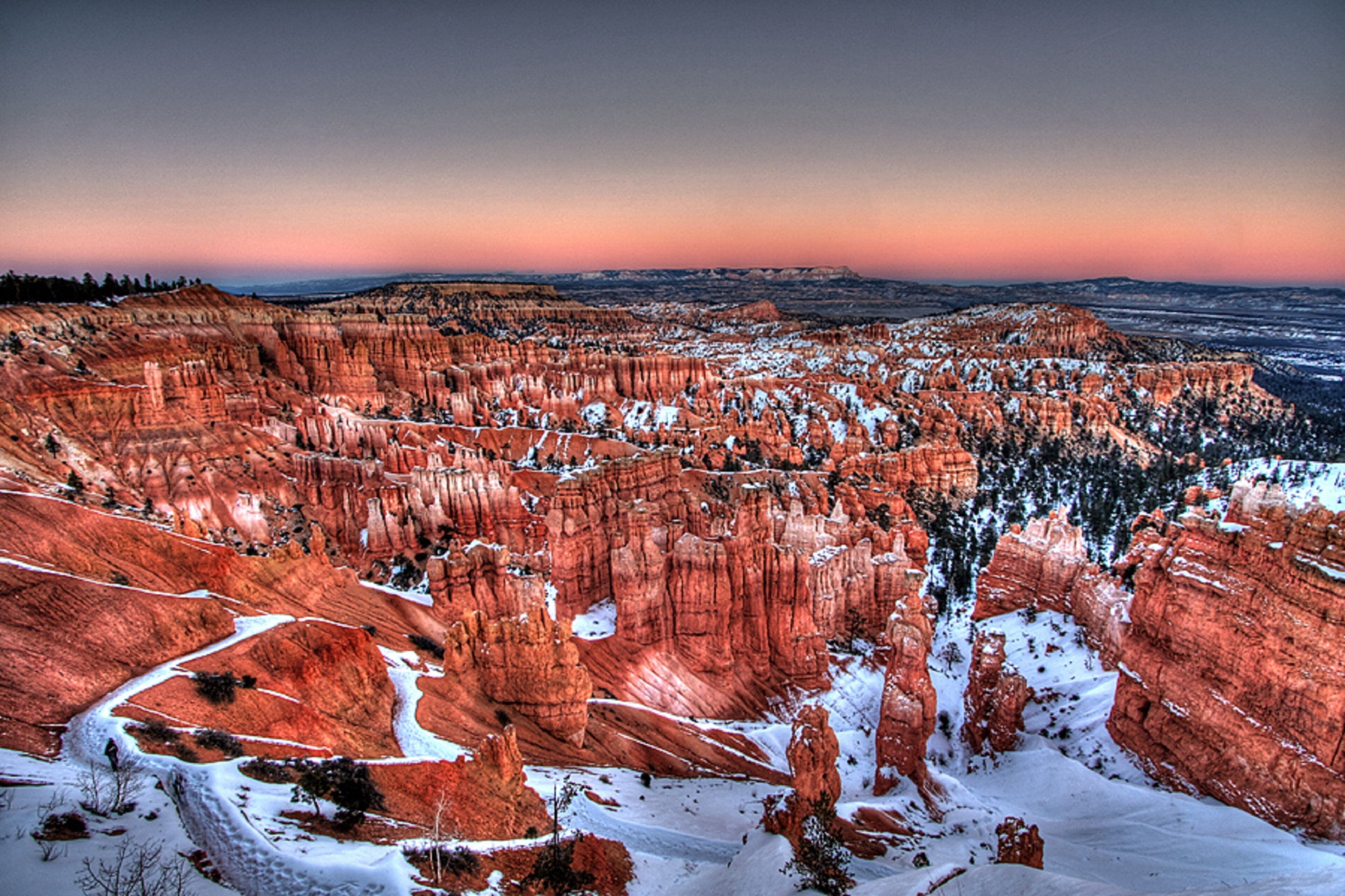 A panoramic view of a rugged canyon landscape with snow-covered terrain and distinctive red rock formations.