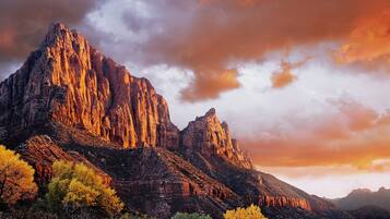 A rugged mountain landscape with prominent rock formations and autumn-colored trees.
