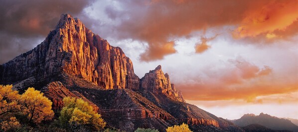A rugged mountain landscape with prominent rock formations and autumn-colored trees.