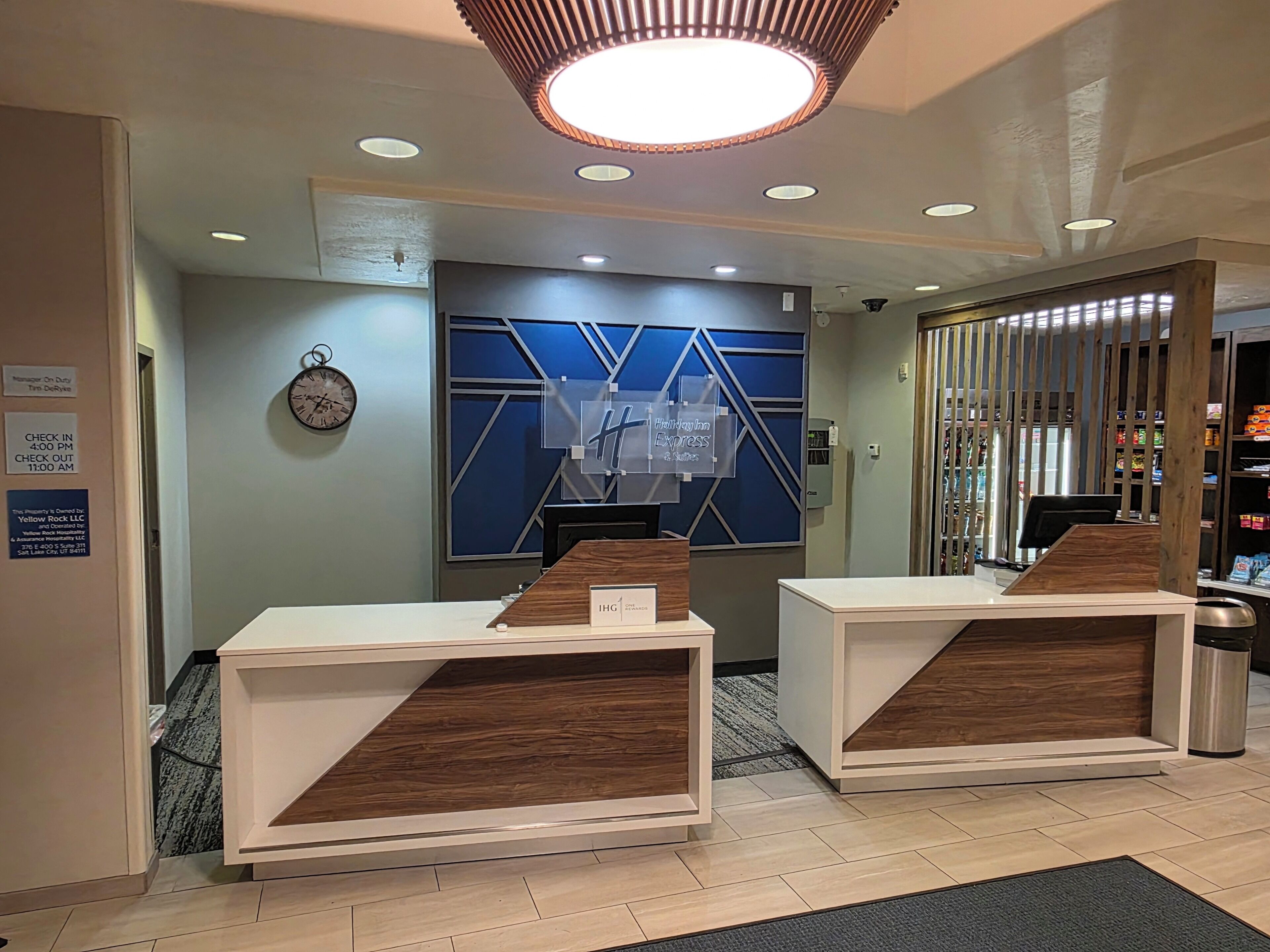 A hotel reception area with a modern design, including a reception desk, a clock, and a sign indicating the hotel's name.