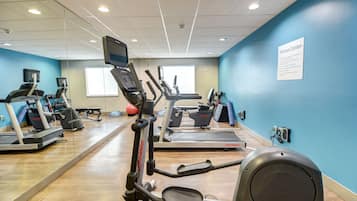 Un gimnasio con cintas de correr, elípticas y un espejo grande.