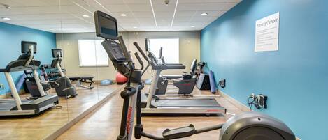 Un gimnasio con cintas de correr, elípticas y un espejo grande.