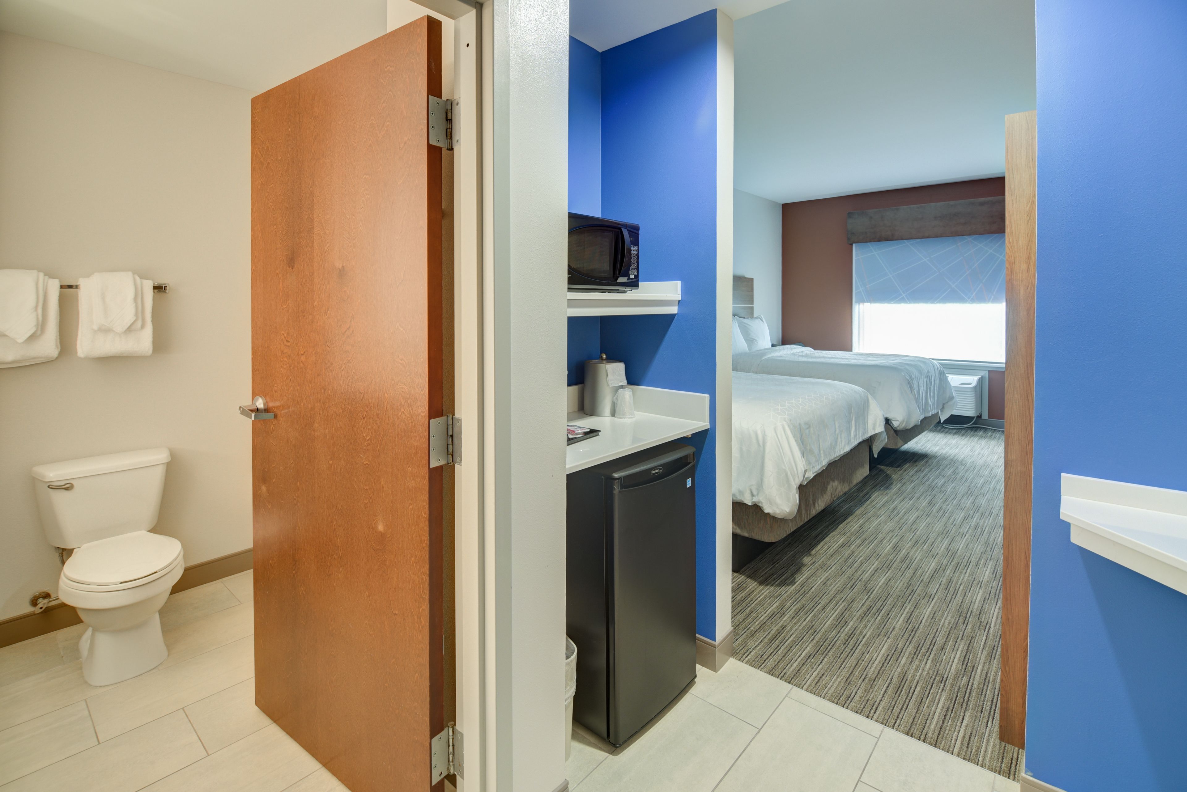 A hotel room with a bathroom, a kitchenette, and a bed.