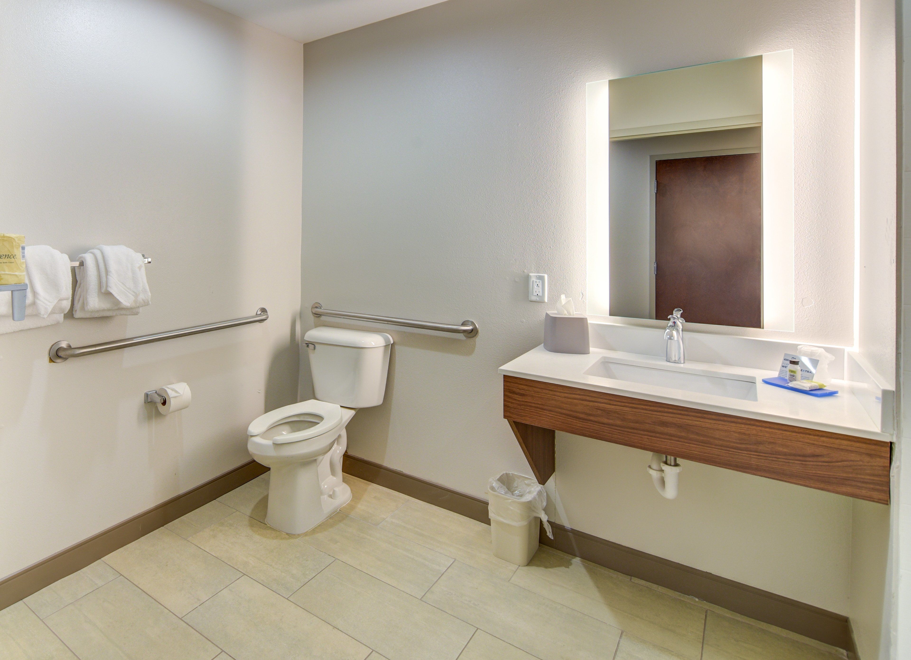 Un baño moderno con inodoro, barras de apoyo, lavabo y espejo.