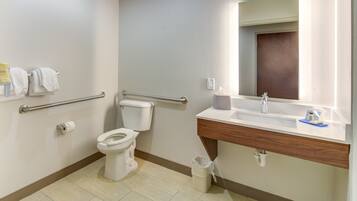Un baño moderno con inodoro, barras de apoyo, lavabo y espejo.