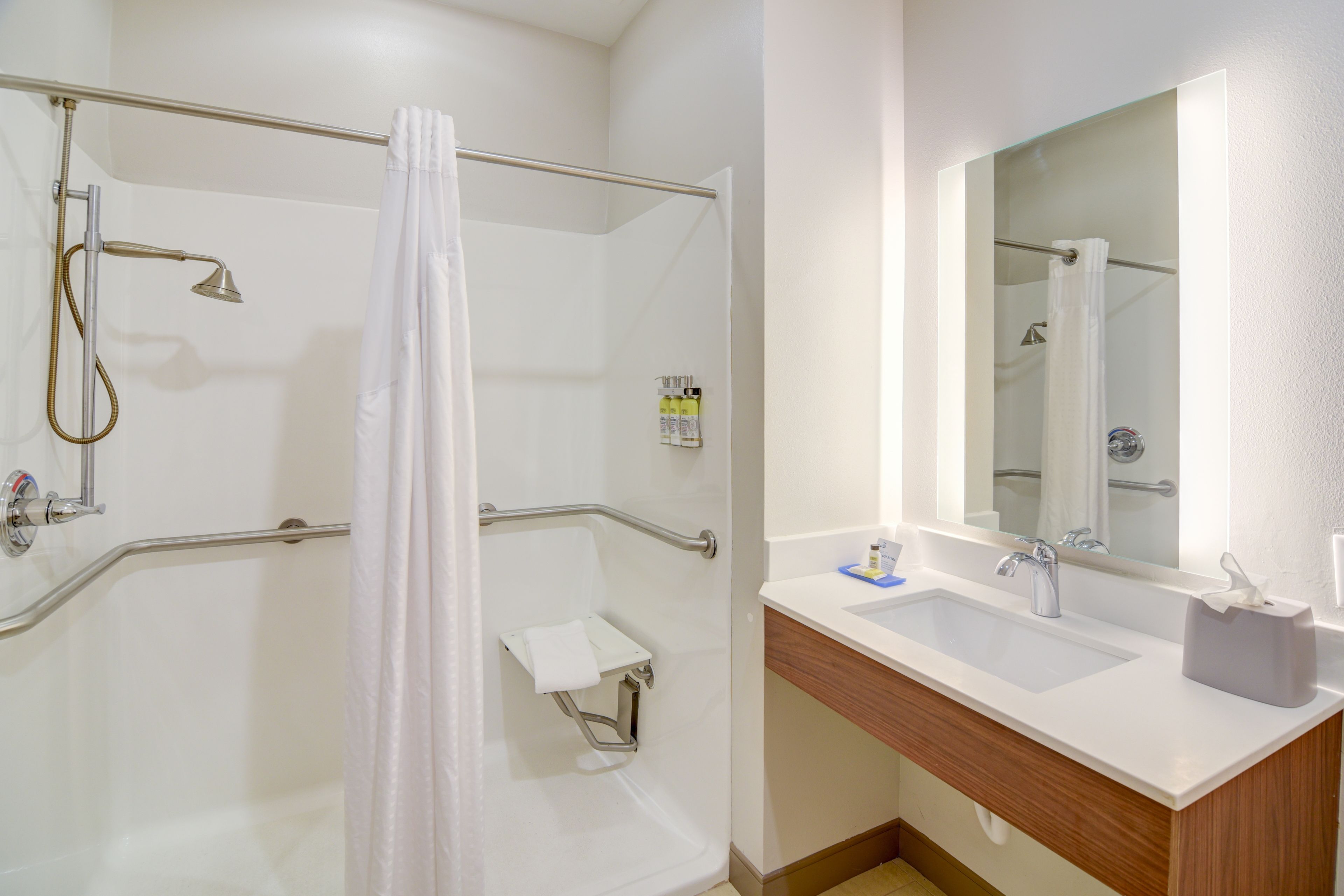 Un baño moderno con ducha a nivel, barras de apoyo, tocador con lavabo y espejo.