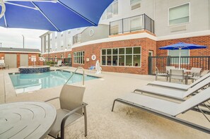 A pool area with lounge chairs and umbrellas, a brick building with large windows, and a small pool. - Holiday Inn Express & Suites Foley by IHG (Foley)