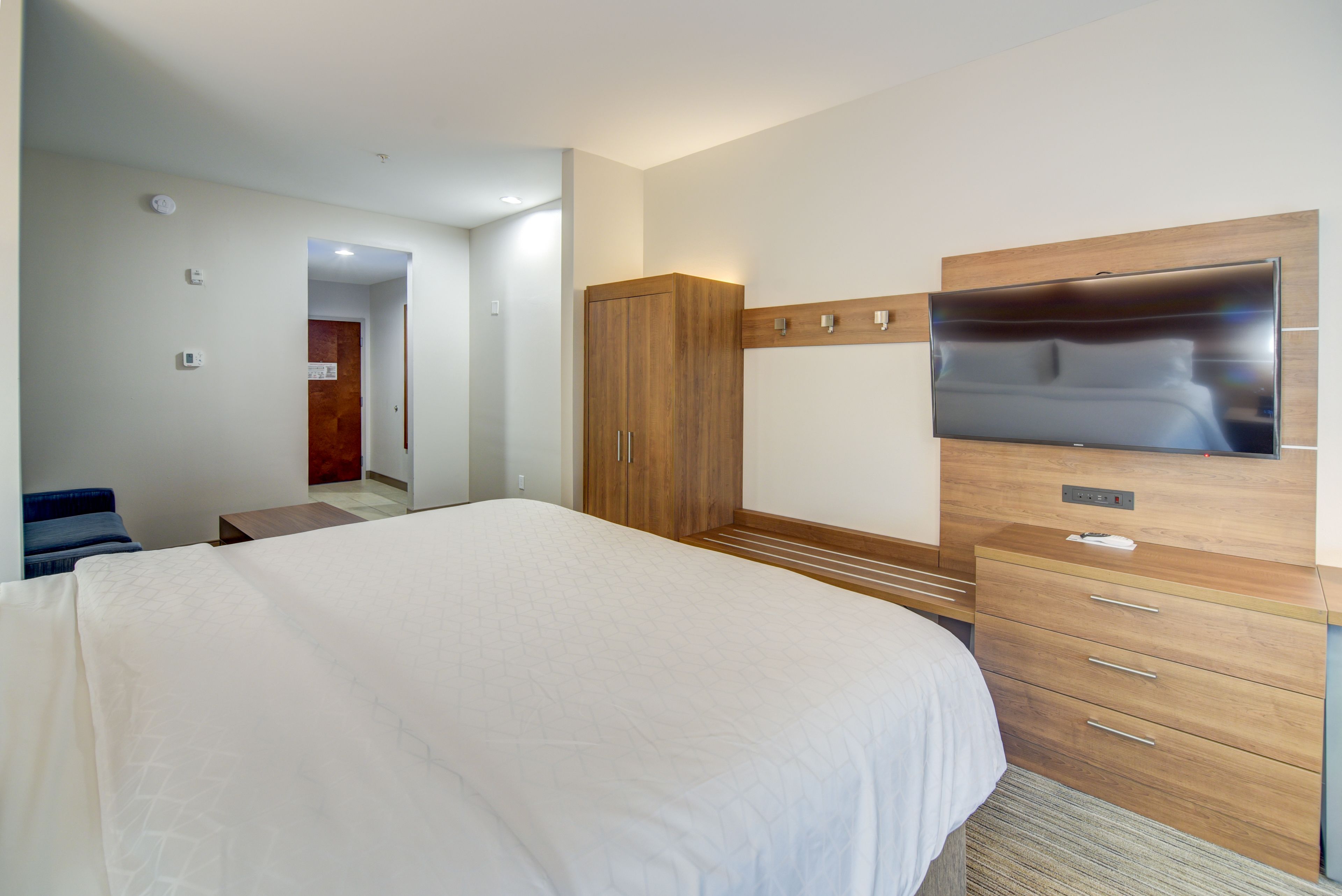 A hotel room with a large bed, a wooden wardrobe, a flat-screen TV, and a small table.
