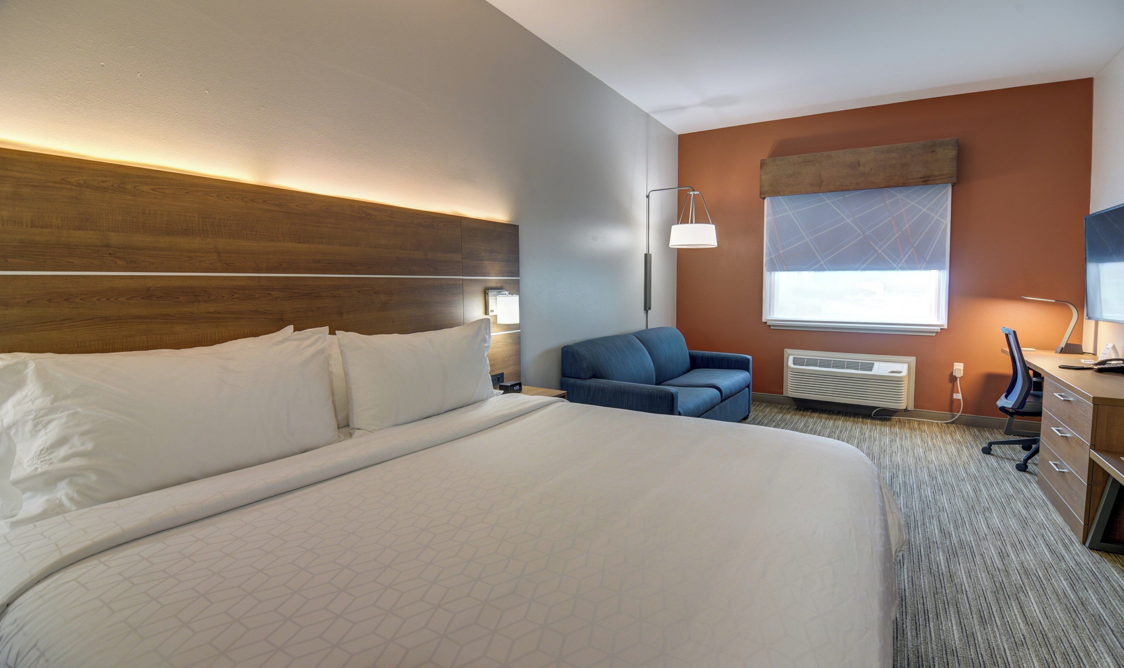 A hotel room with a large bed, a desk with a chair, a TV, and a window with blinds.