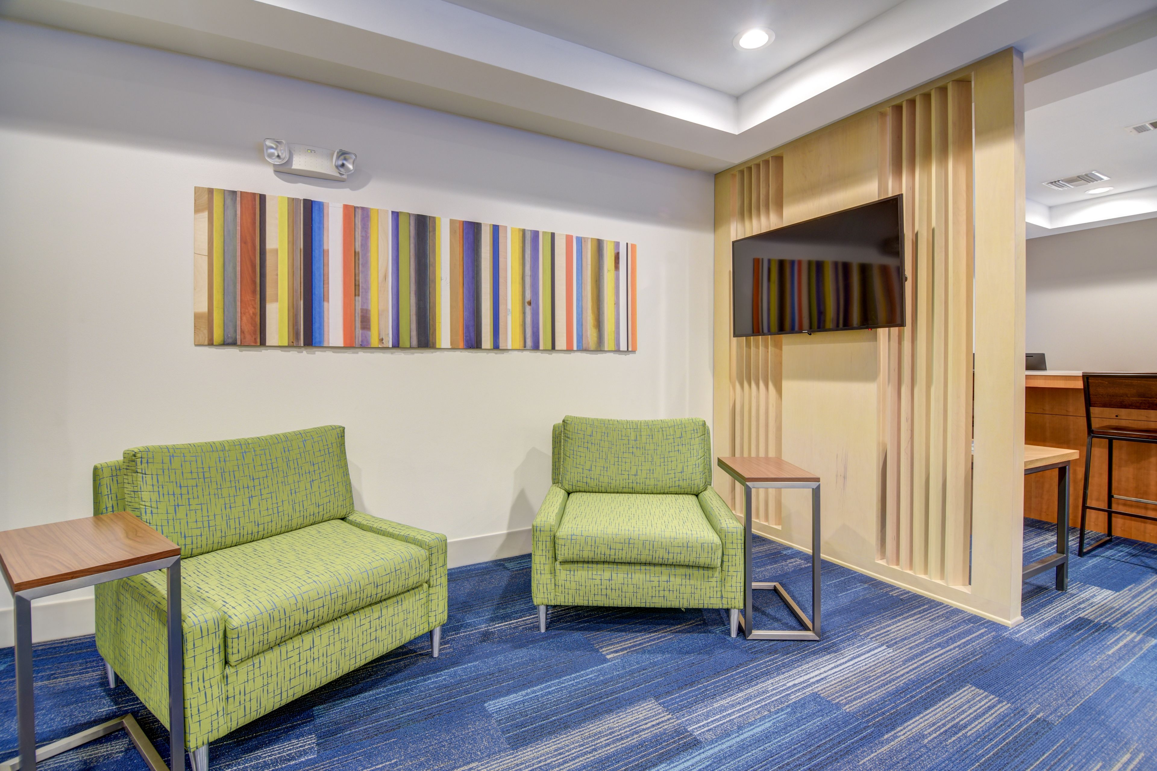 A room with two green armchairs, a small wooden table, a colorful abstract painting, and a TV on a wooden stand.