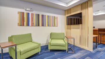 A room with two green armchairs, a small wooden table, a colorful abstract painting, and a TV on a wooden stand.