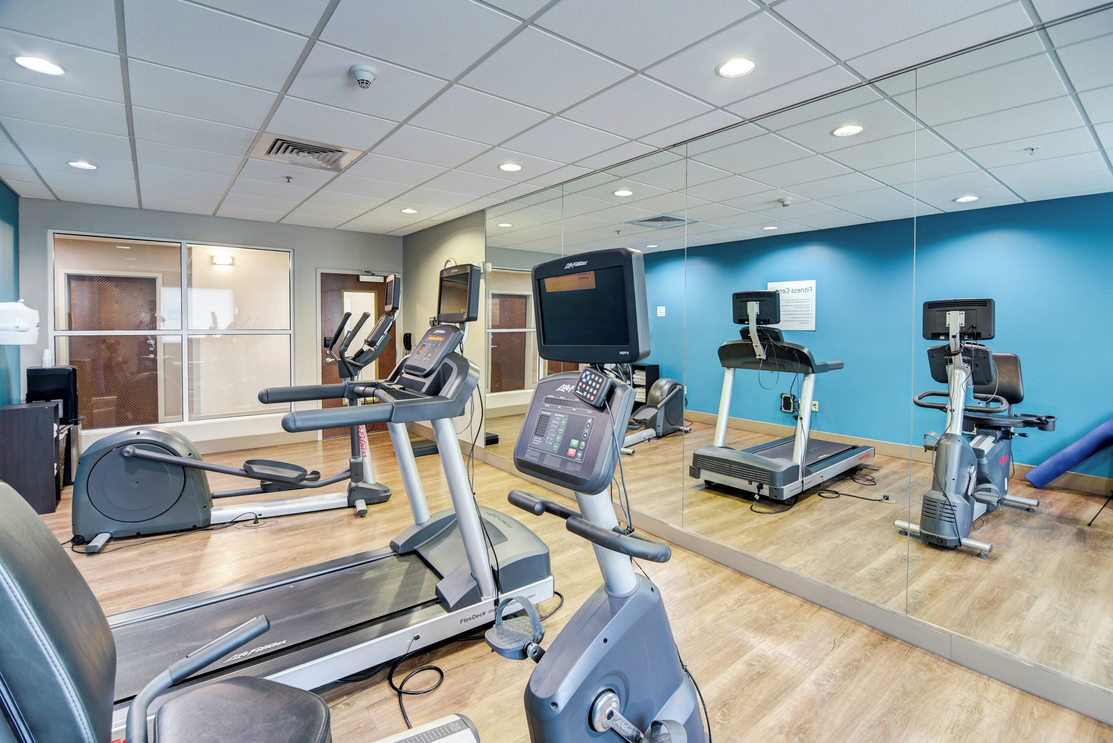 Un gimnasio con varias máquinas de cardio, un espejo grande y una pared de acento azul.