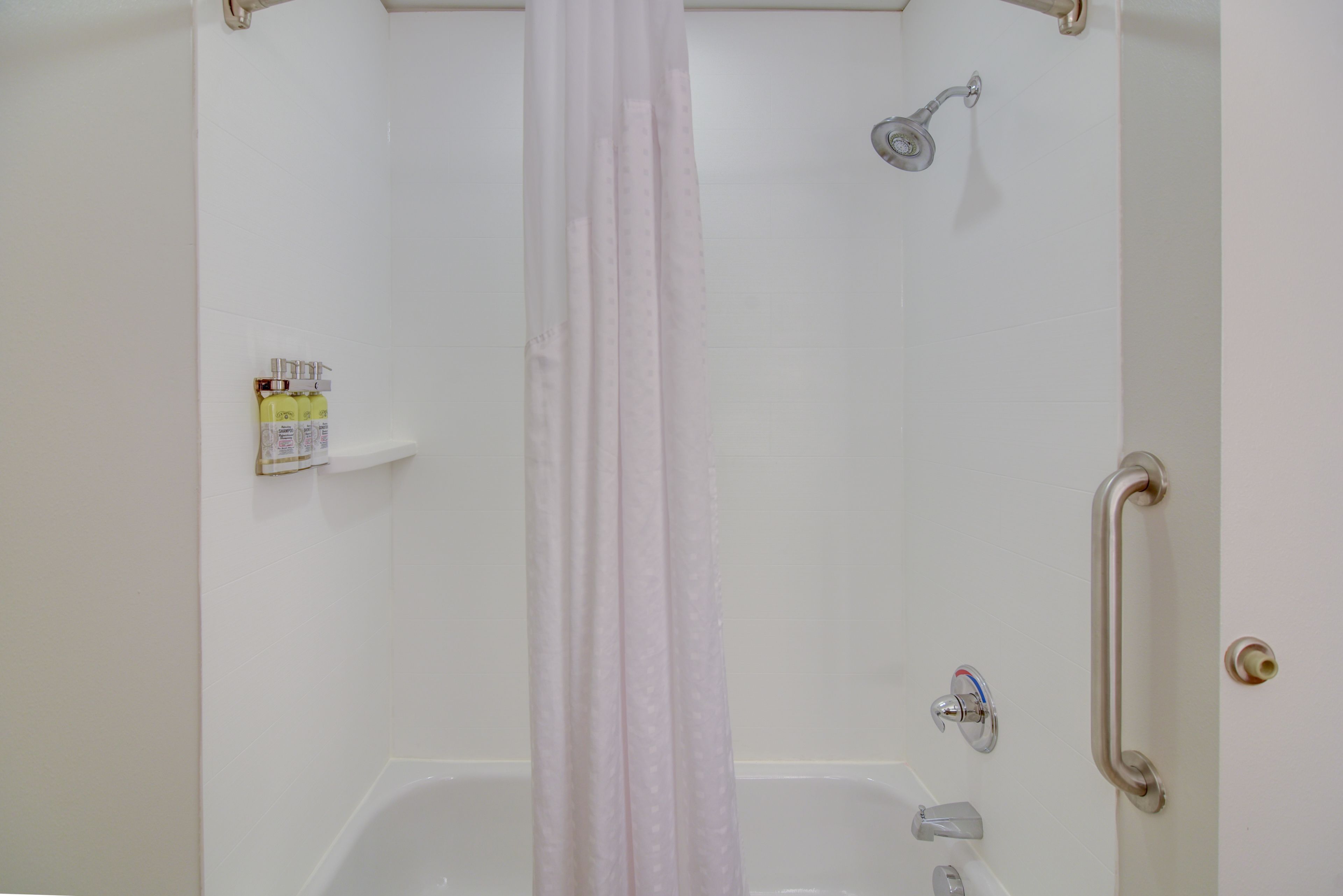 A shower with a curtain, a grab bar, and a shelf with toiletries.