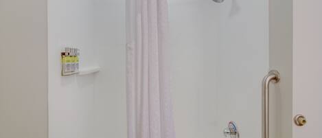 A shower with a curtain, a grab bar, and a shelf with toiletries.