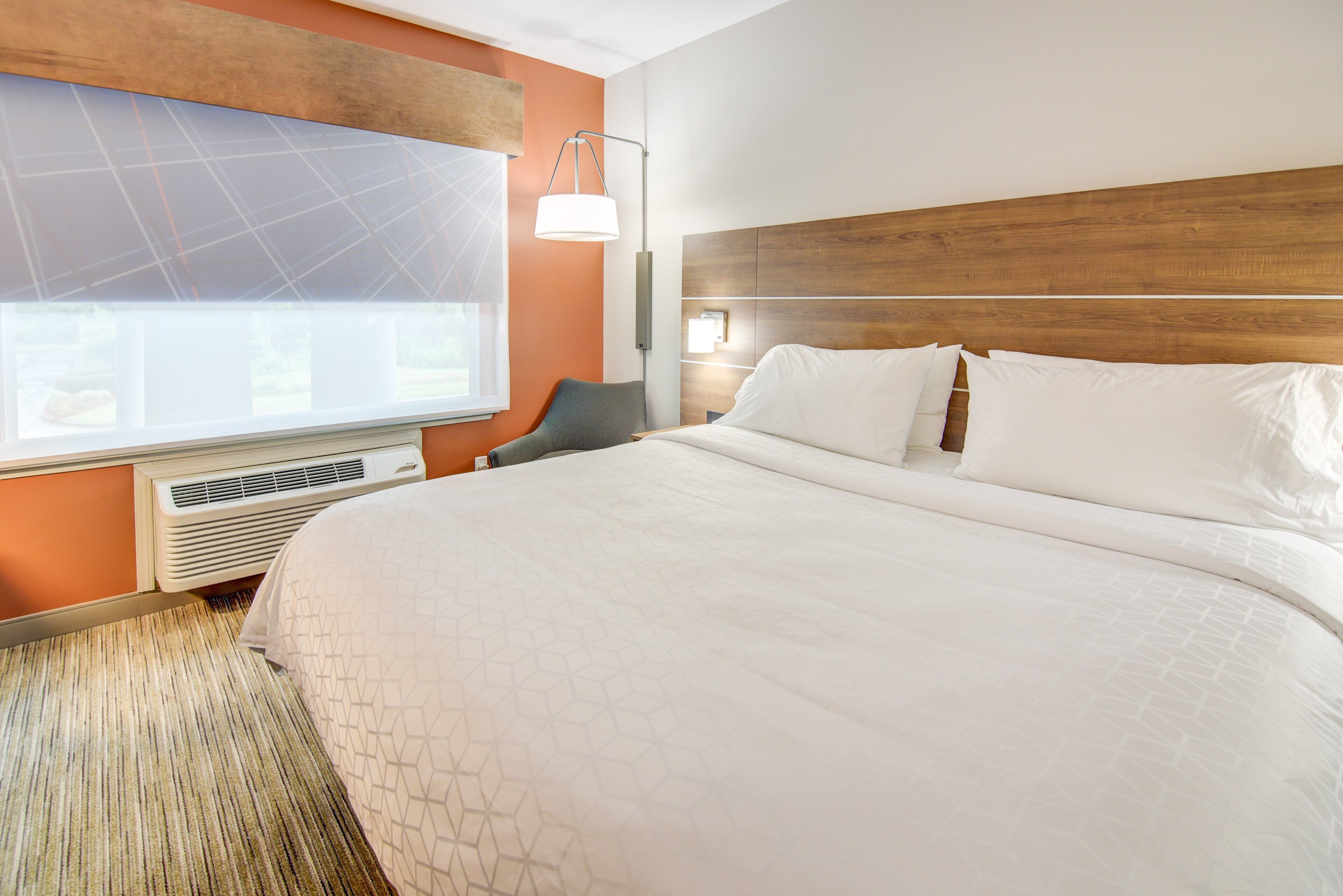 Hotelkamer met een groot bed, een bureau, een stoel, een raam met zonwering en een wandairconditioner.