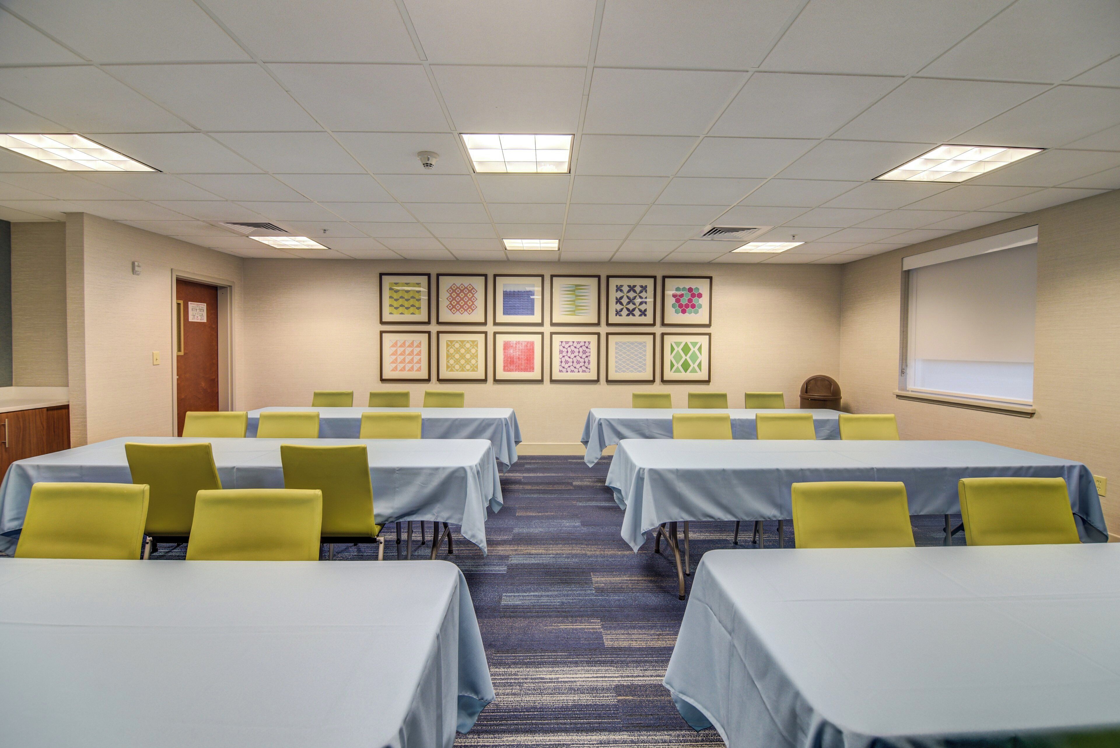 A conference room with tables and chairs, a projector screen, and framed artwork on the wall.
