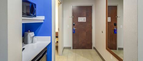 A hallway with a microwave on a shelf, a door with a lock, and a mirror on the wall.