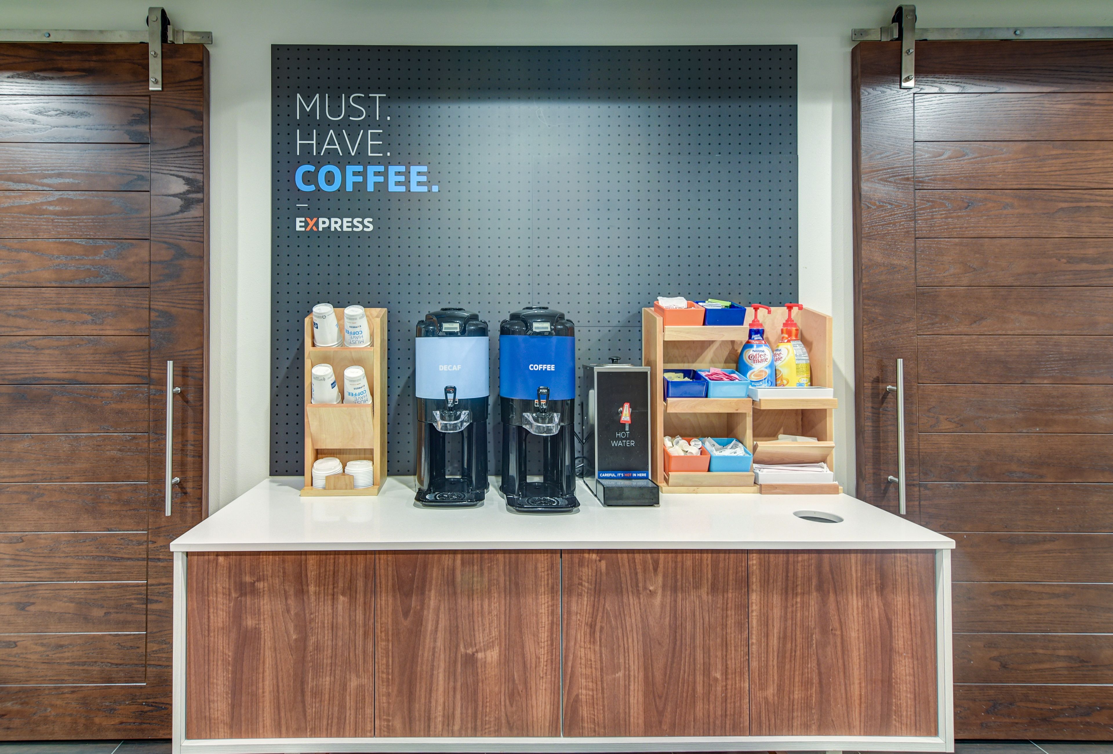 A coffee station with multiple coffee makers and a sign that reads "MUST HAVE COFFEE."