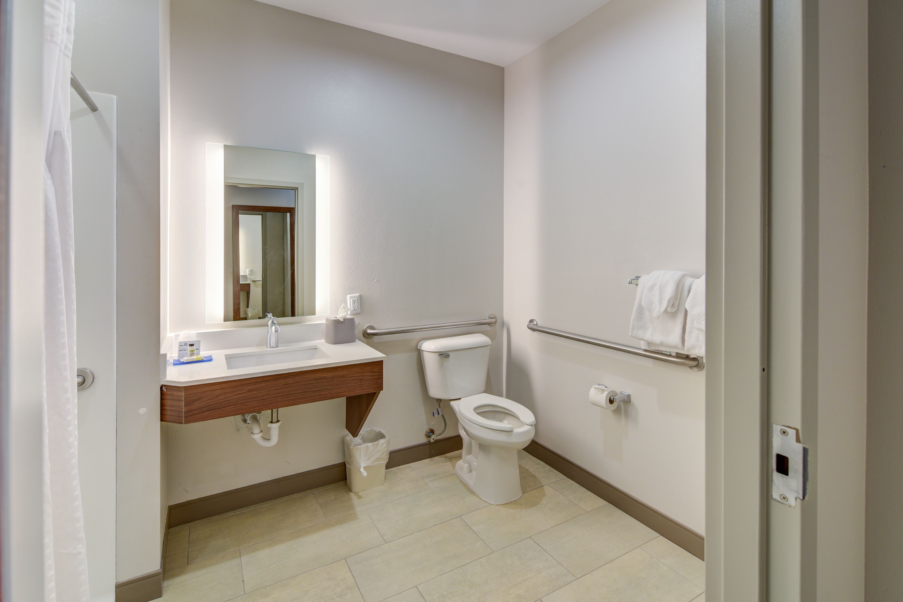 A bathroom with a white sink, mirror, toilet, and handrail.