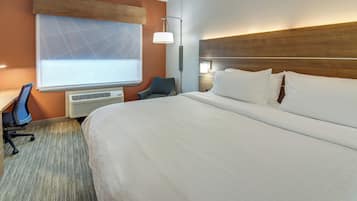Habitación de hotel con una cama grande, un escritorio, una silla, aire acondicionado instalado en la pared y una pantalla de proyector.