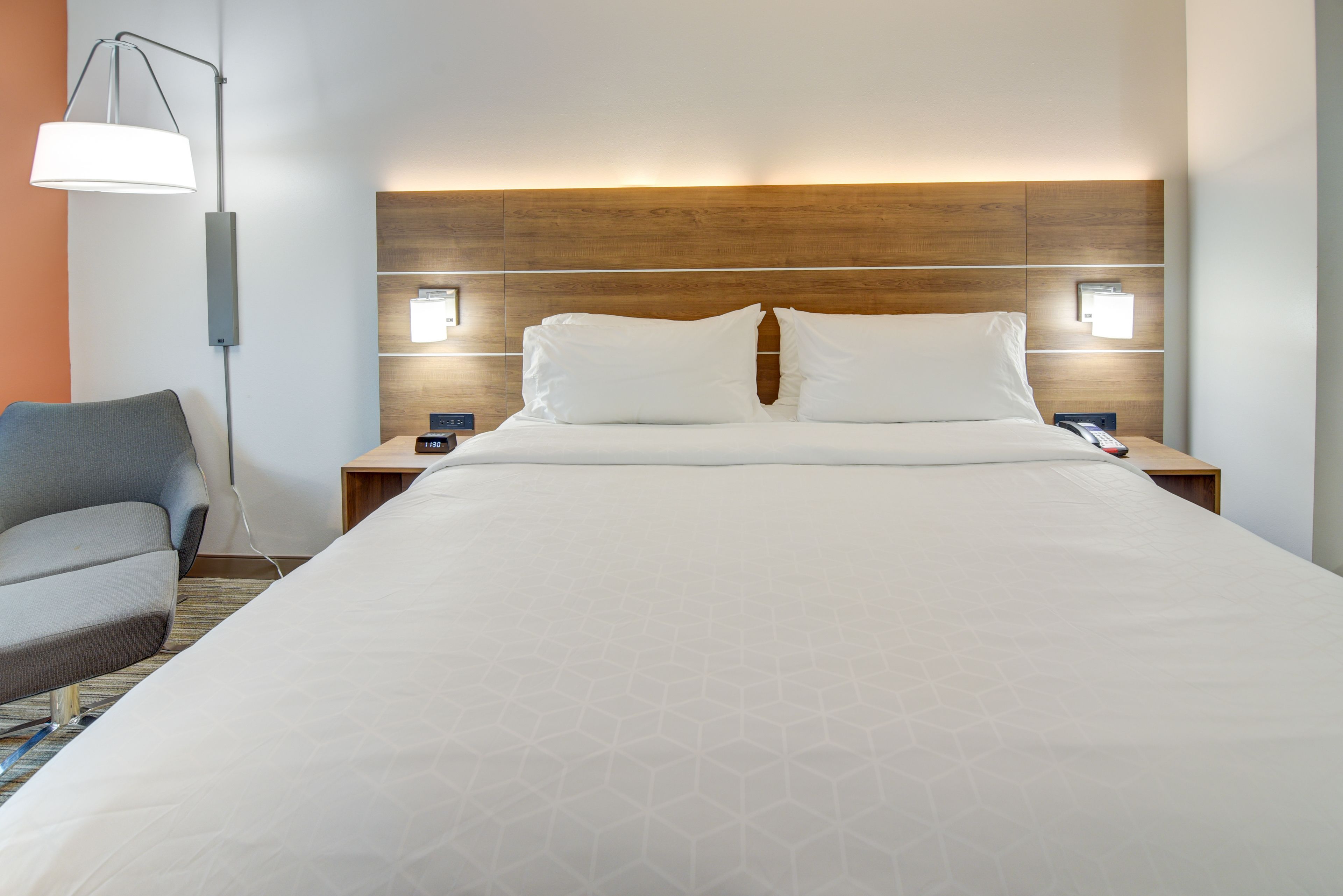 A hotel room with a large bed, two bedside tables, a nightstand, a lamp, and a chair.