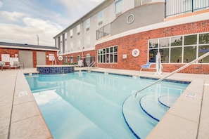 A swimming pool with a clear blue water, surrounded by a brick building with windows and a covered area with chairs. - Holiday Inn Express & Suites Foley by IHG (Foley)