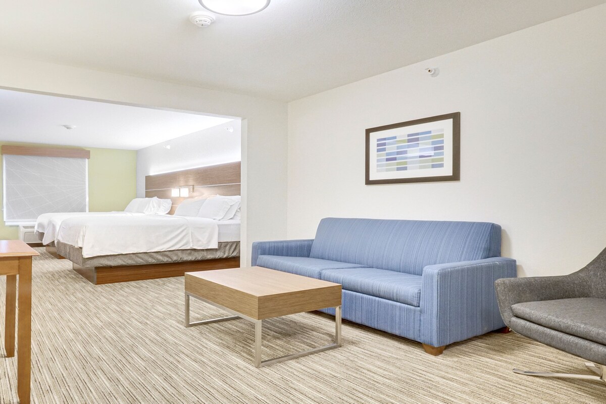 A hotel room with a bed, a blue sofa, a grey armchair, a wooden coffee table, and a framed picture on the wall.