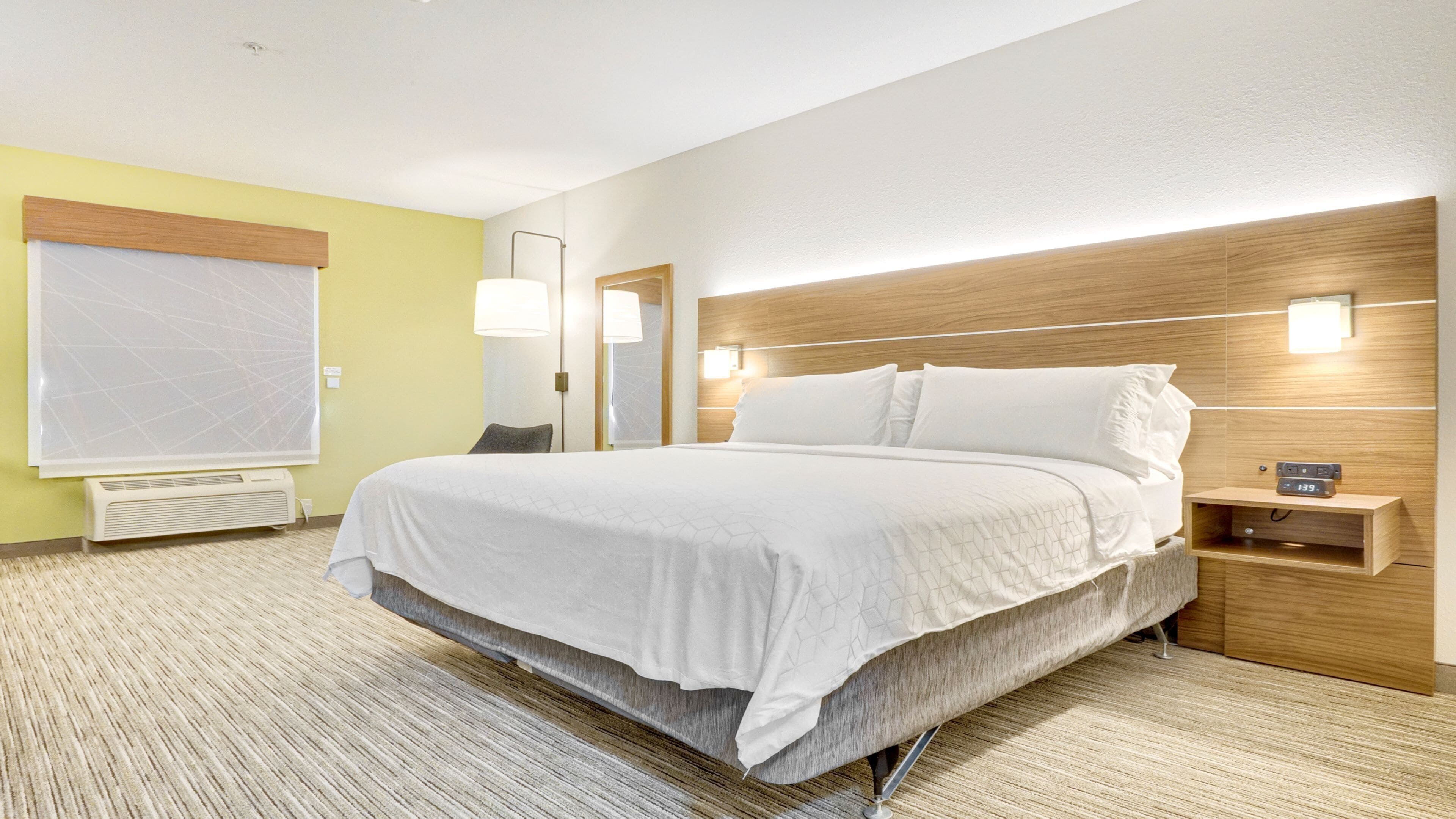 Une chambre d’hôtel avec un grand lit, des tables de chevet, une lampe fixée au mur et une fenêtre avec des stores.