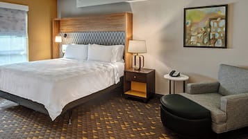 Una habitación de hotel con cama, mesita de noche, lámpara, silla y una obra de arte en la pared.