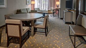 Ein Hotelzimmer mit einem runden Esstisch, zwei Stühlen, einer Couch, einem Fernseher und einem Schreibtisch mit Stuhl.