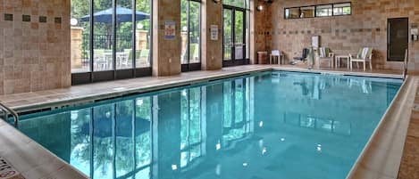 A swimming pool with clear water, surrounded by tiled walls and large windows.