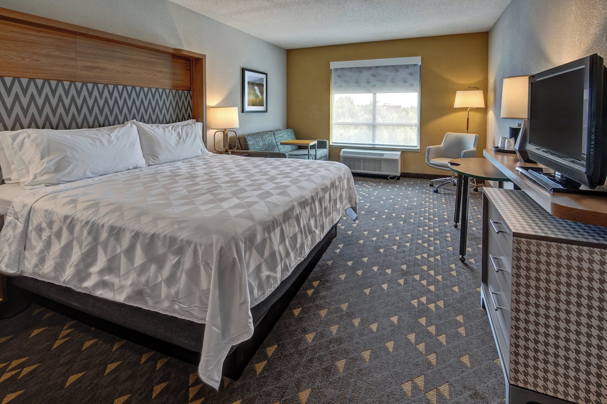 A hotel room with a large bed, a desk, a television, and a window.