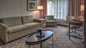 Una camera d'albergo con un divano, una poltrona, un tavolino con una lampada e una finestra con tende.