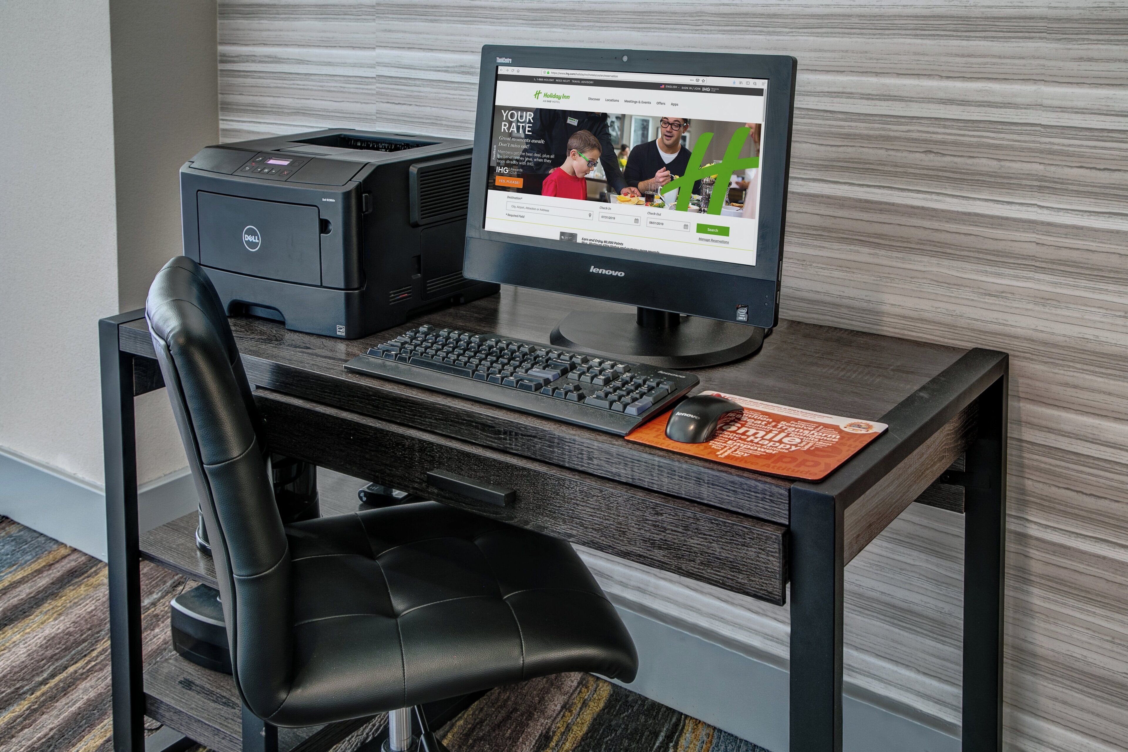 Ein Hotel-Schreibtisch mit einem Desktop-Computer, einem Drucker und einer Tastatur.